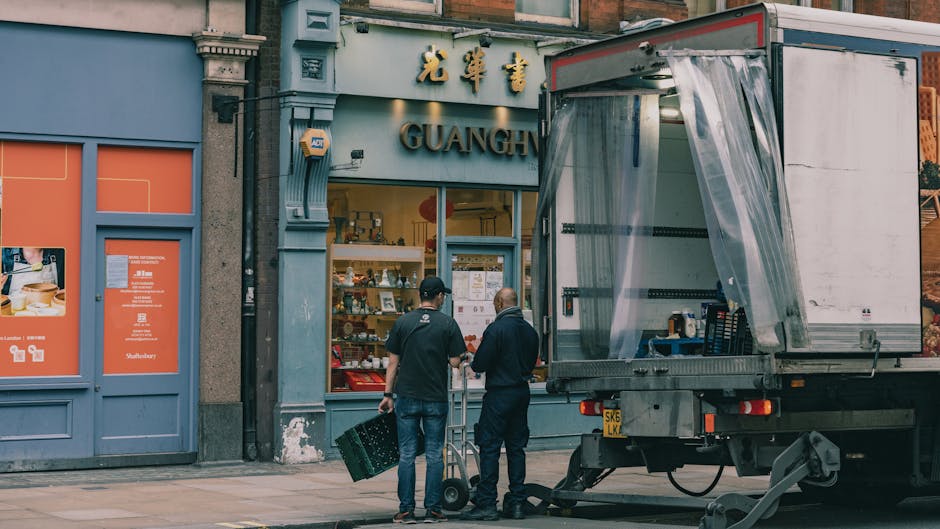 Two removal personnel are engaged in the loading process outside a commercial premises on Fulham Road, Brompton, during a house or business relocation operated by Removals Brompton. One worker is hold