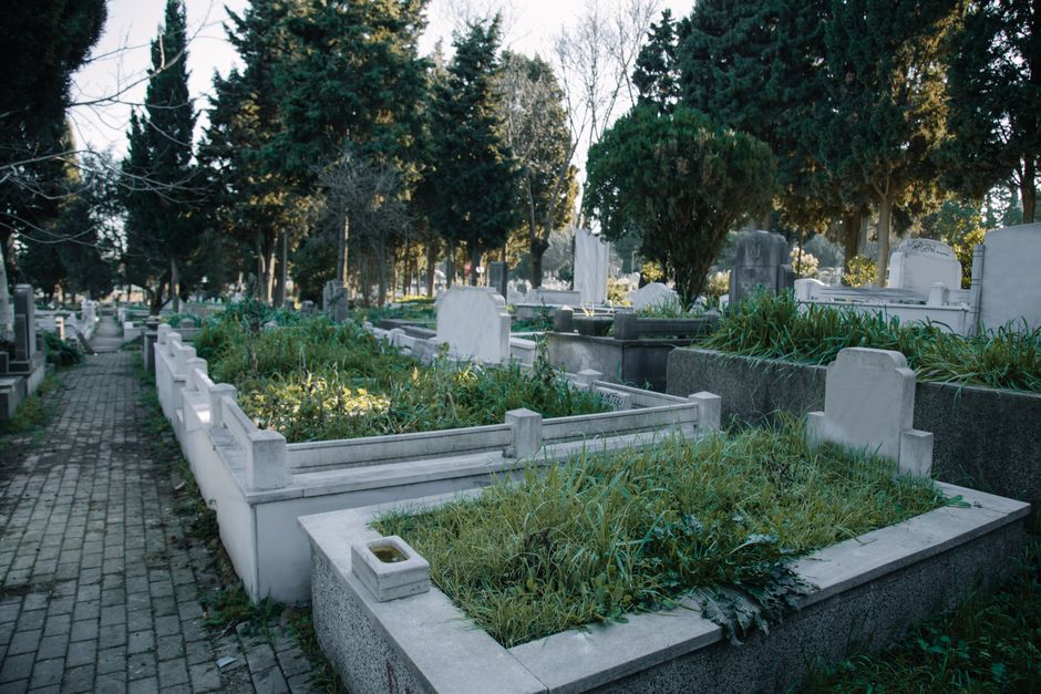 A wide view of a memorial structure within Brompton Cemetery, featuring a prominent stone domed tower at the top center, surrounded by a colonnade with arched openings. In front of the structure, ther